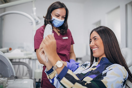 A young woman in a dental chair inspects her smile in a mirror